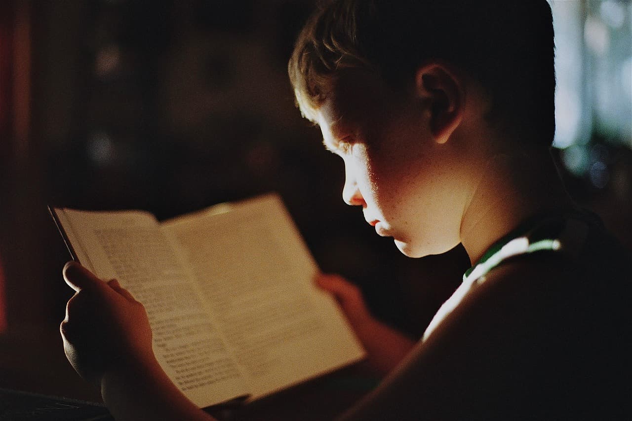 Young child wearing glasses while reading a colorful book, smiling, bright and warm setting