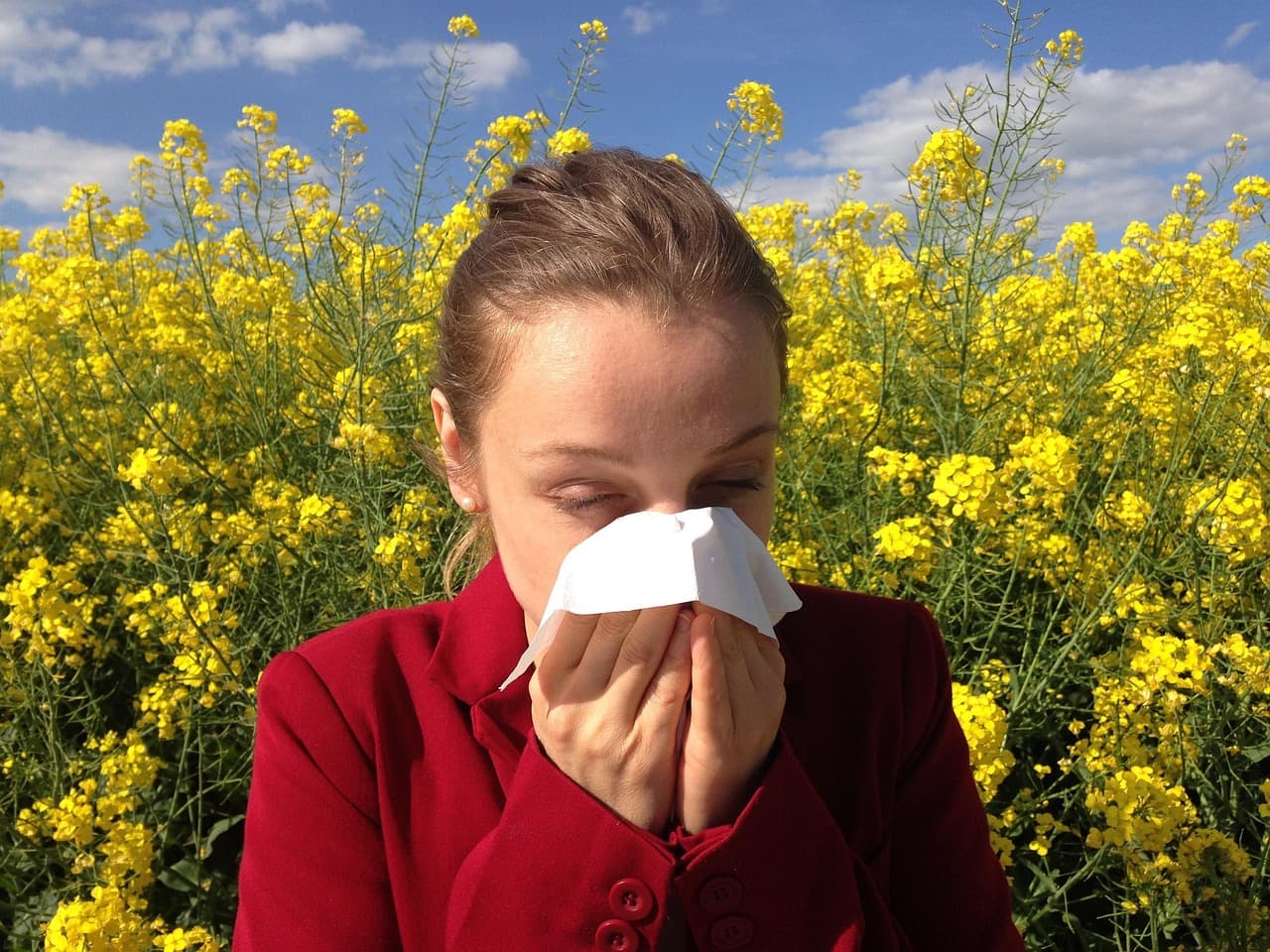 Young child sneezing outdoors with eyes closed, springtime background with pollen in the air