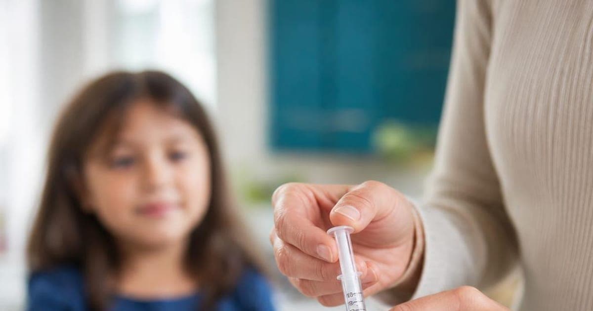 Parent measuring children's liquid allergy medicine with an oral dosing syringe at the kitchen counter