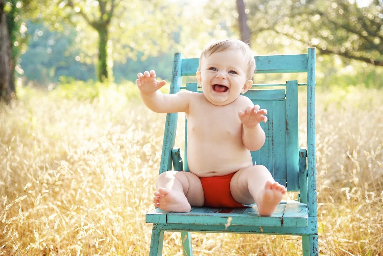 Toddler sitting in a high chair turning away from food, parent looking on patiently at the dinner table