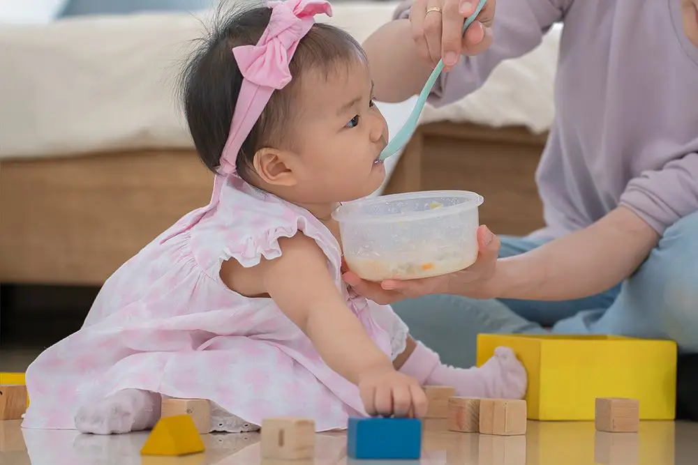 mother feeding baby while she plays with wooden blocks