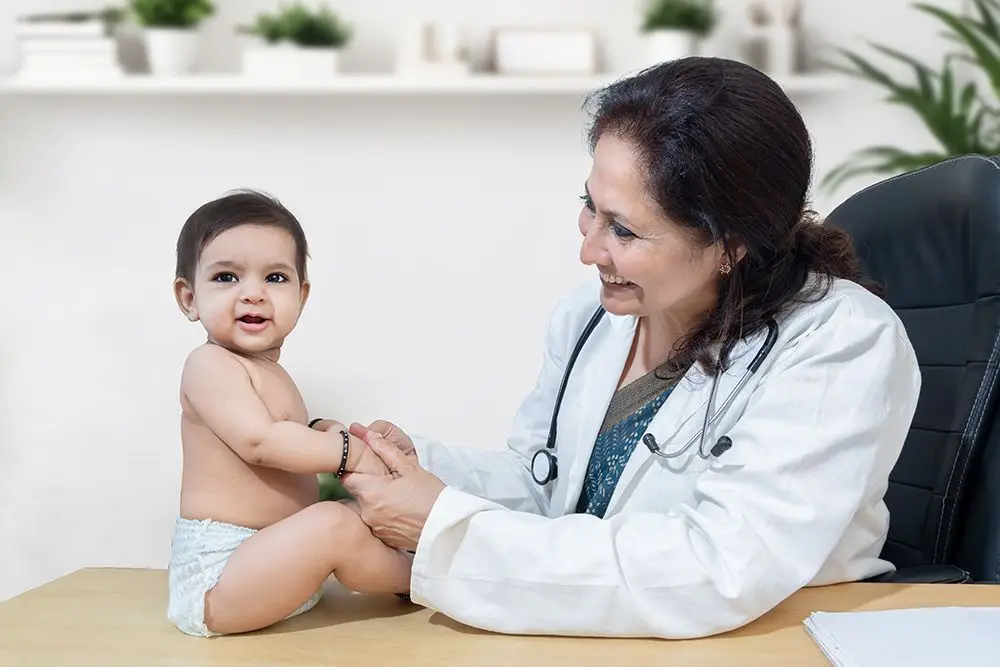 pediatrician smiling at a baby sitting on a table in front of her